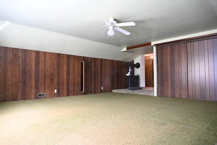 Sloped ceiling, wood paneling, ceiling fan, and built-in wood-finish sliding doors