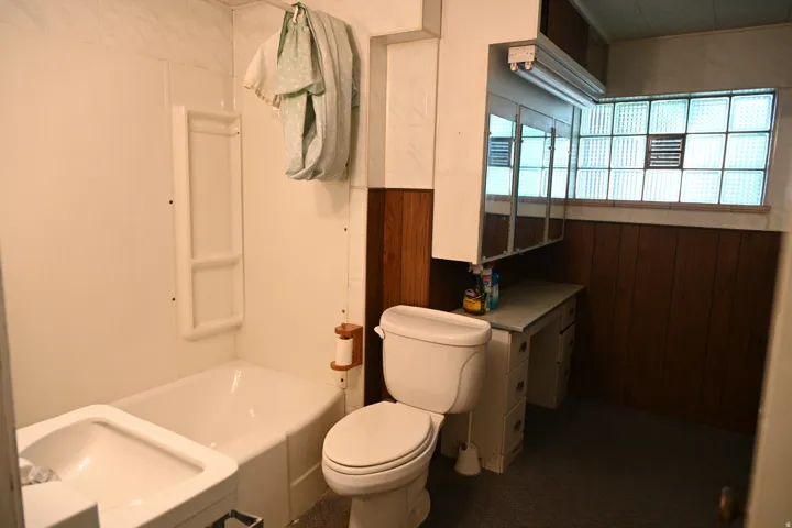 Bathtub with white surround, toilet, vanity with built-in storage, mirrored medicine cabinet, and glass block window
