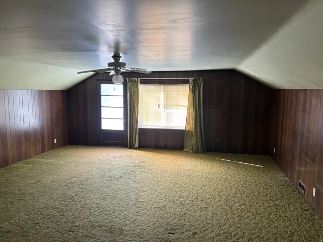 Sloped ceilings with a ceiling fan, paneled walls, and wall-to-wall carpeting