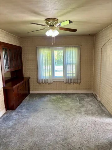 Window with natural light, ceiling fan with light fixture, built-in wooden cabinetry, textured wall coverings