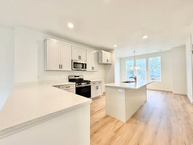 Modern kitchen featuring light cabinetry, stainless steel appliances, quartz countertops, a kitchen island with sink, and wood-finish flooring