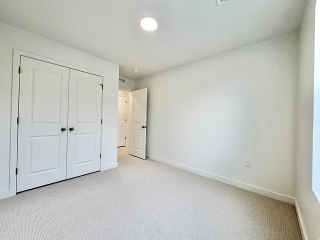 Light-colored carpet flooring, white walls, and a flush-mount ceiling light