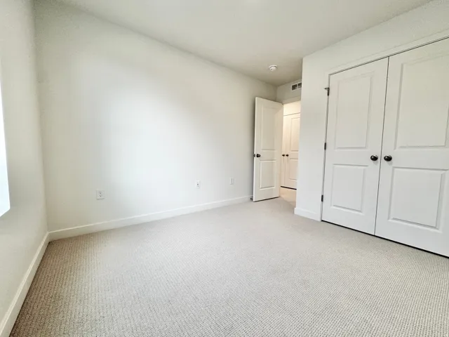 Neutral-toned carpeting, white walls, and white bi-fold closet doors with black hardware
