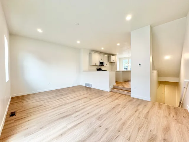 Open-concept living area featuring wood-finish flooring, recessed lighting, white walls, and a partial wall separating a kitchen with light cabinetry