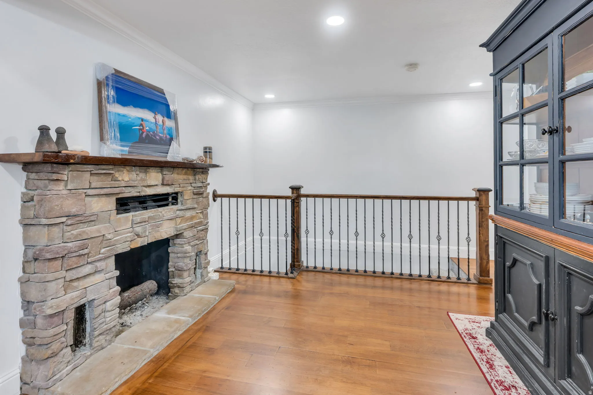 Stone-clad fireplace with a wood mantel, wood-finish flooring, and wrought iron railing with wood newel posts