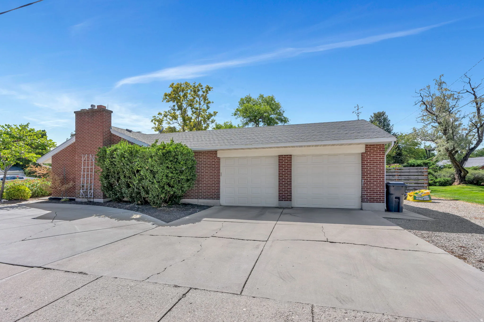 Red brick exterior with a two-car garage, asphalt shingle roof, and mature landscaping