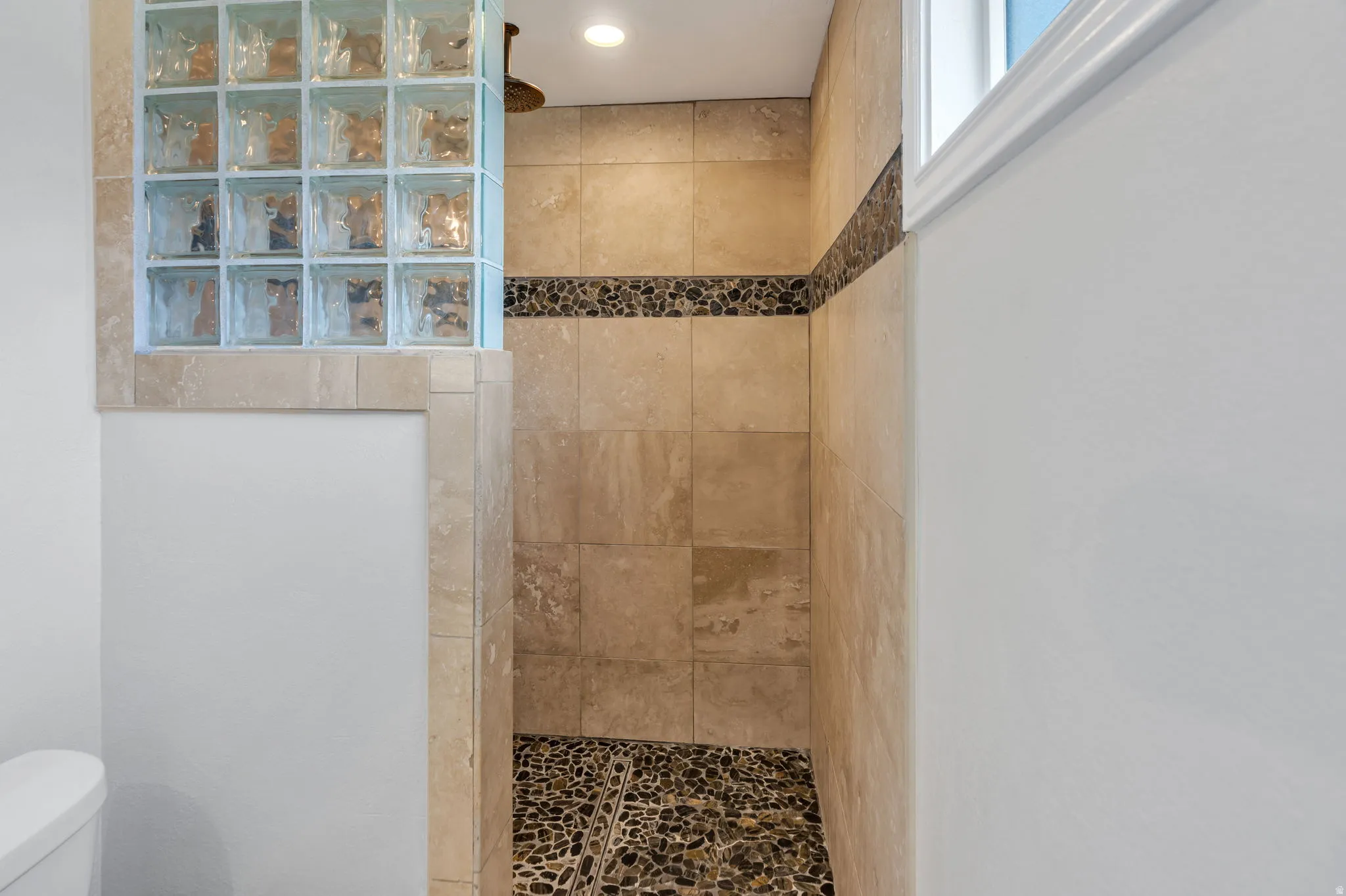 Tiled shower with glass block wall, river rock floor, accent tile band, and recessed lighting