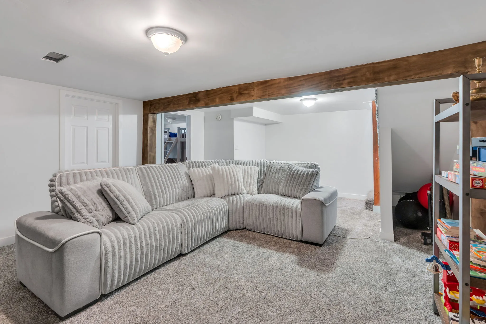 Carpeted living area featuring a prominent wood beam, white painted walls, and ceiling-mounted lighting fixtures