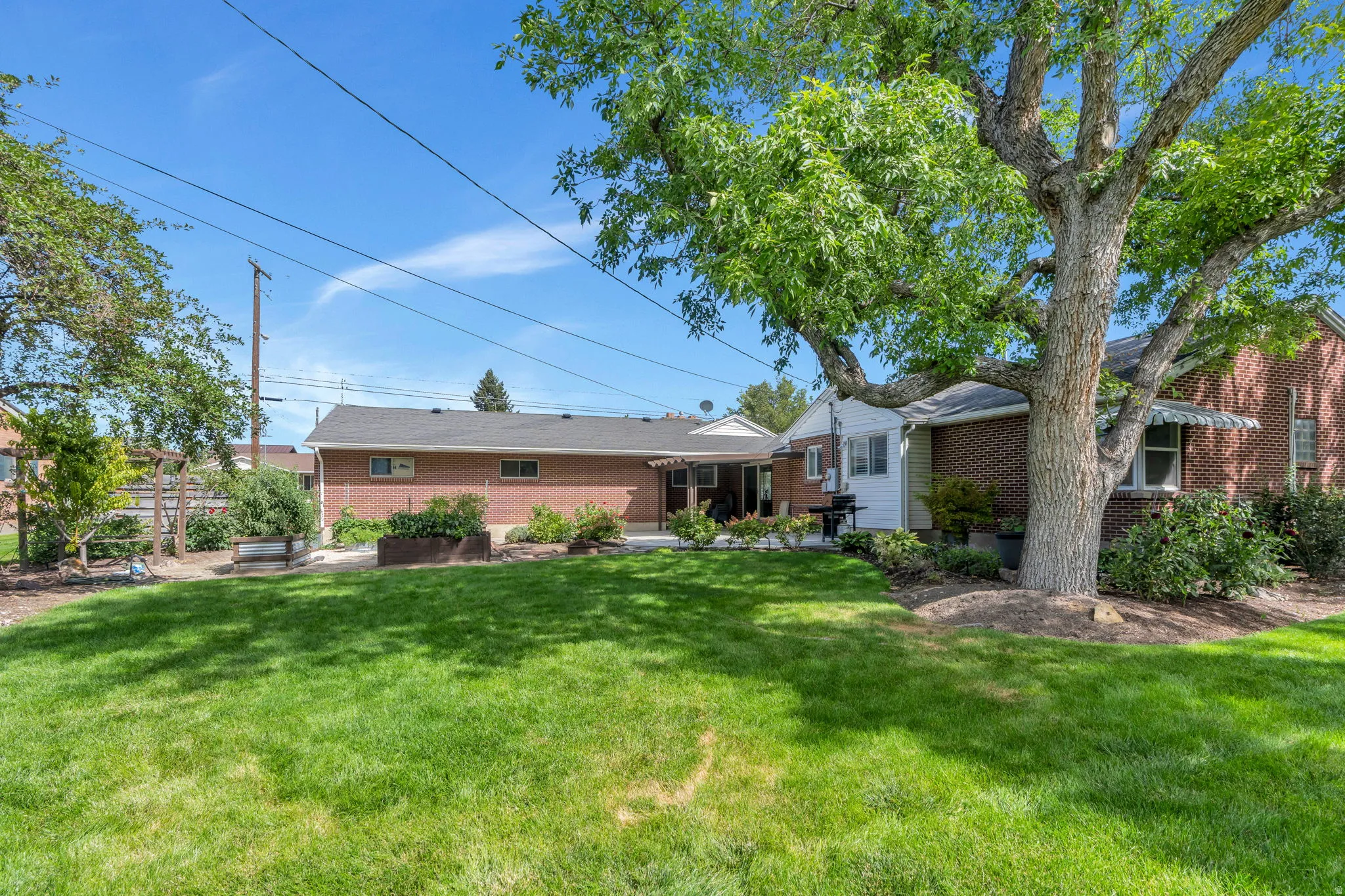 Expansive lawn with mature trees, a red brick exterior, and a covered patio area