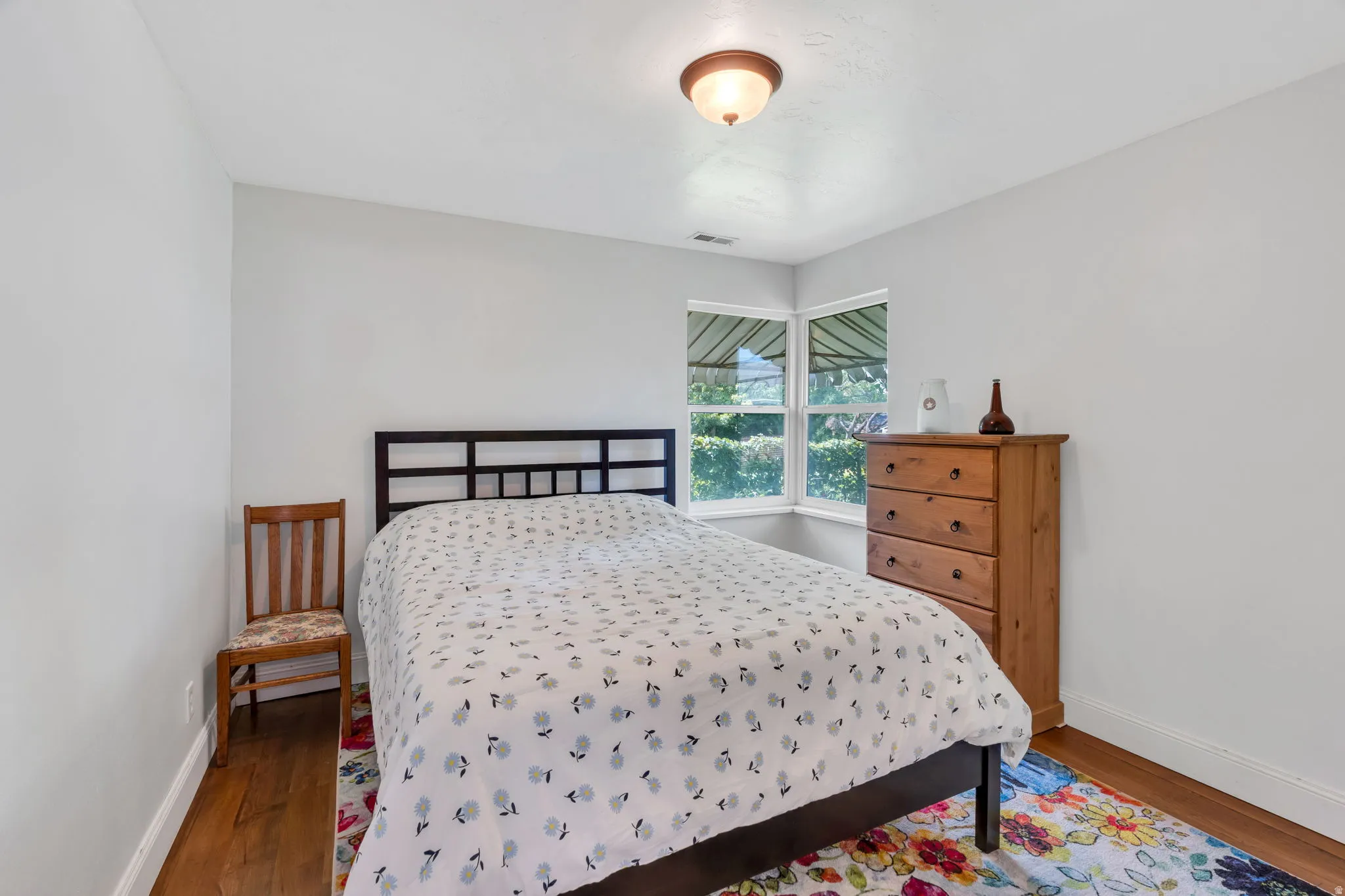 Corner window providing natural light, overhead flush mount light fixture, and wood-finish flooring