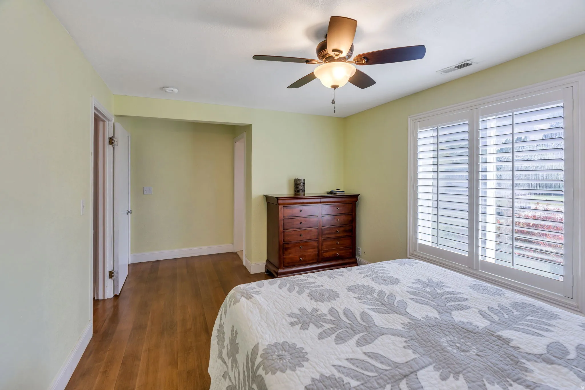 Wood-finish flooring, ceiling fan with integrated lighting, and window with plantation shutters