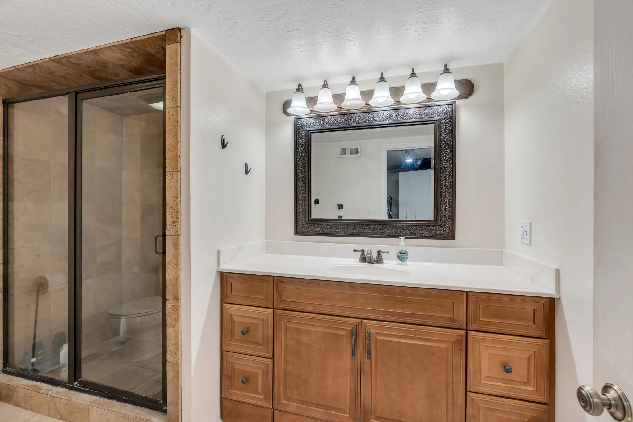 Glass-enclosed shower with tile surround, wood-finish vanity with countertop, framed mirror, and a 5-light fixture