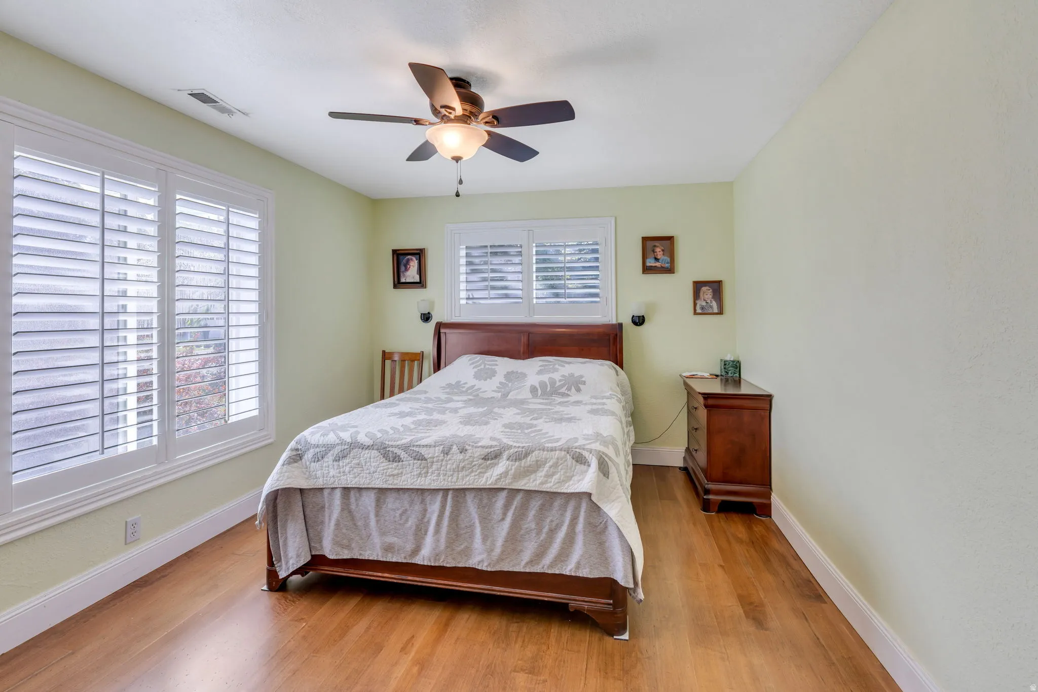 Hardwood flooring, two windows with plantation shutters, ceiling fan with integrated lighting, and light-toned walls