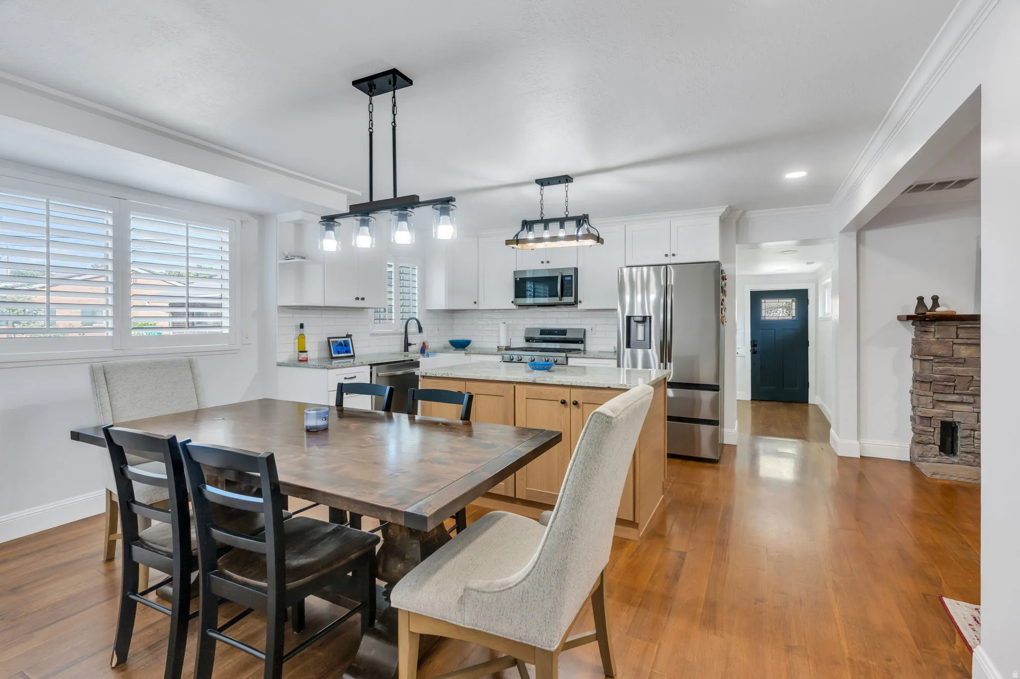 Open-concept kitchen and dining area featuring hardwood flooring, a central island with a light wood base, white shaker-style cabinetry, and stainless steel appliances