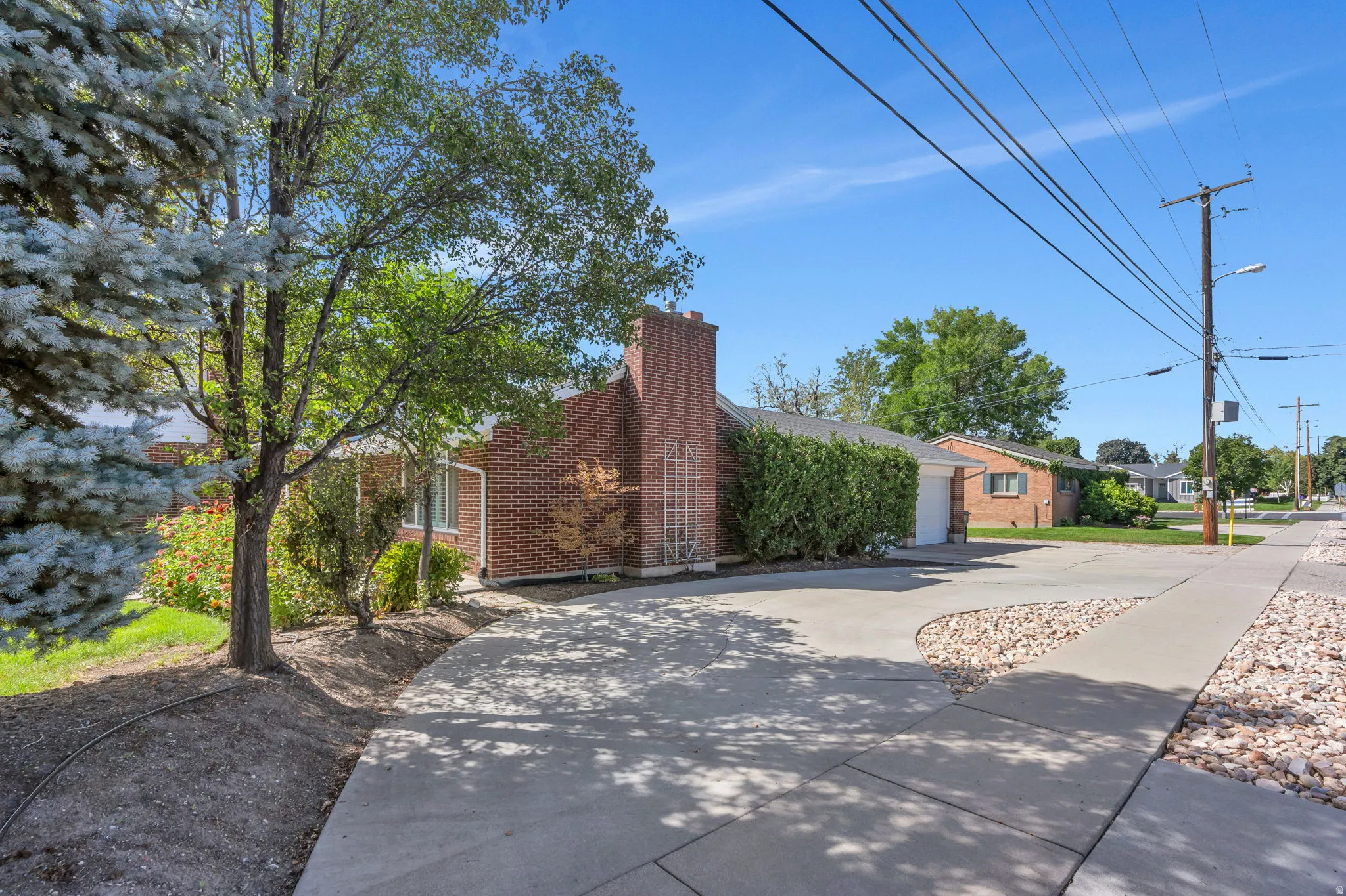 Brick exterior, mature trees, concrete driveway, lush landscaping, and a street-facing garage
