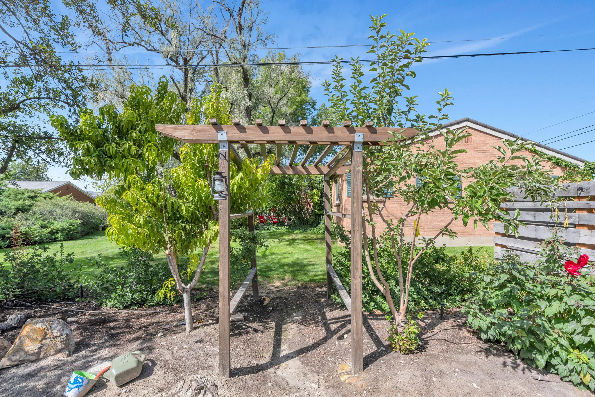 Landscaped outdoor area featuring a wooden arbor, established trees, and green lawn