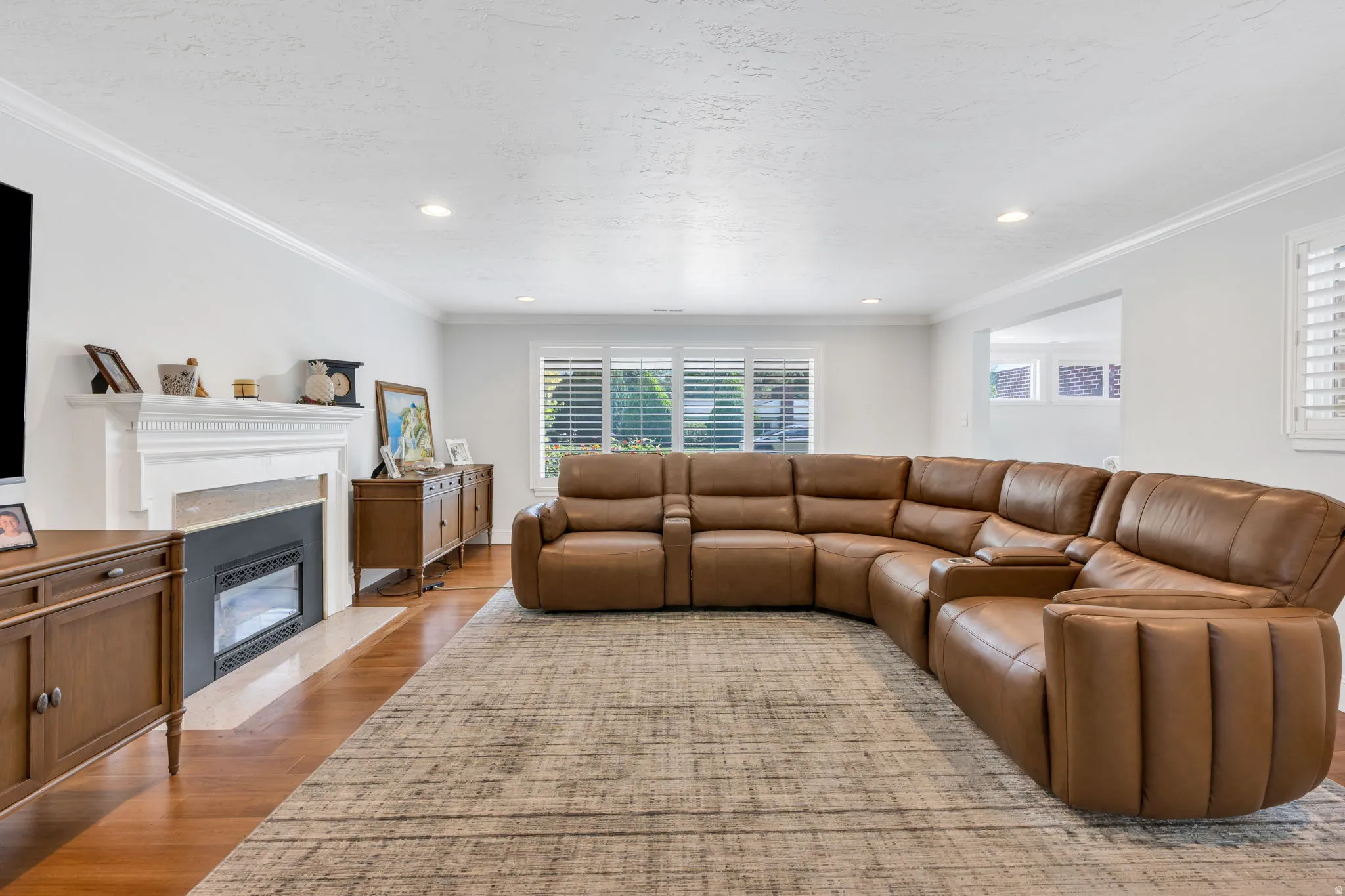 Hardwood flooring, recessed lighting, crown molding, white fireplace with hearth, white window shutters