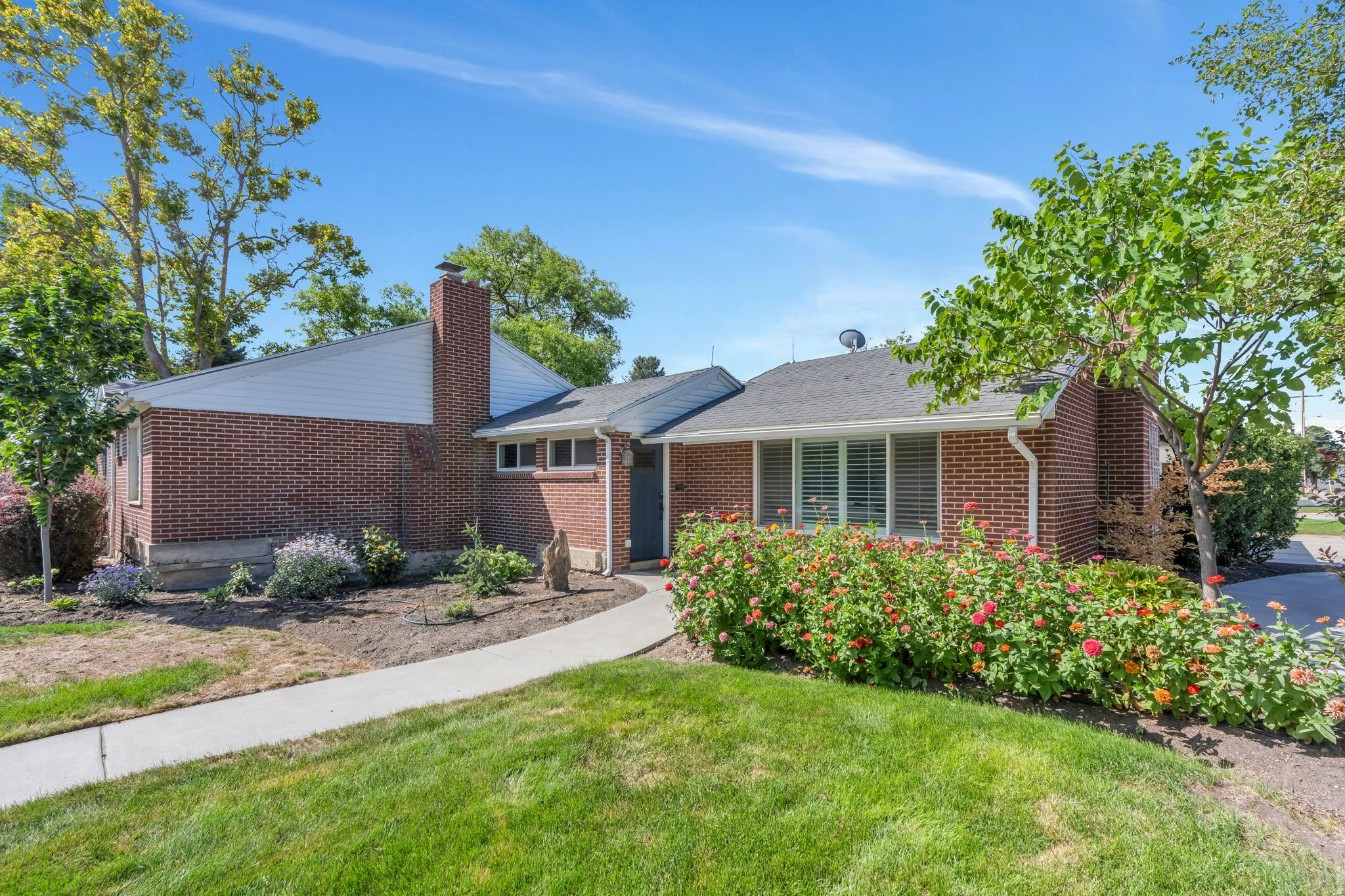 Brick exterior with a prominent chimney, mature landscaping, established lawn, and a concrete pathway
