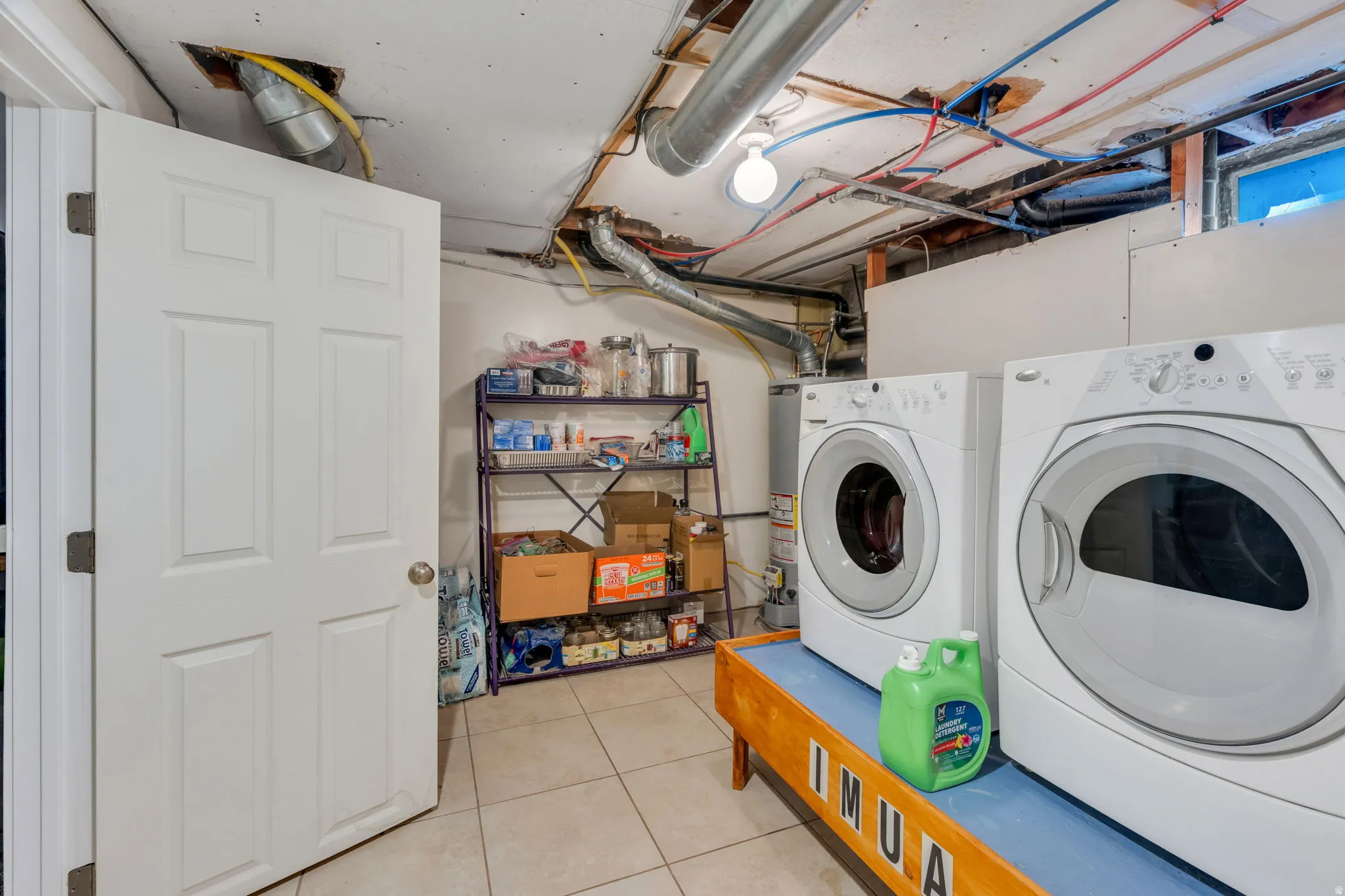 Tiled flooring, white paneled door, exposed ceiling utilities, washer and dryer appliances, metal shelving unit