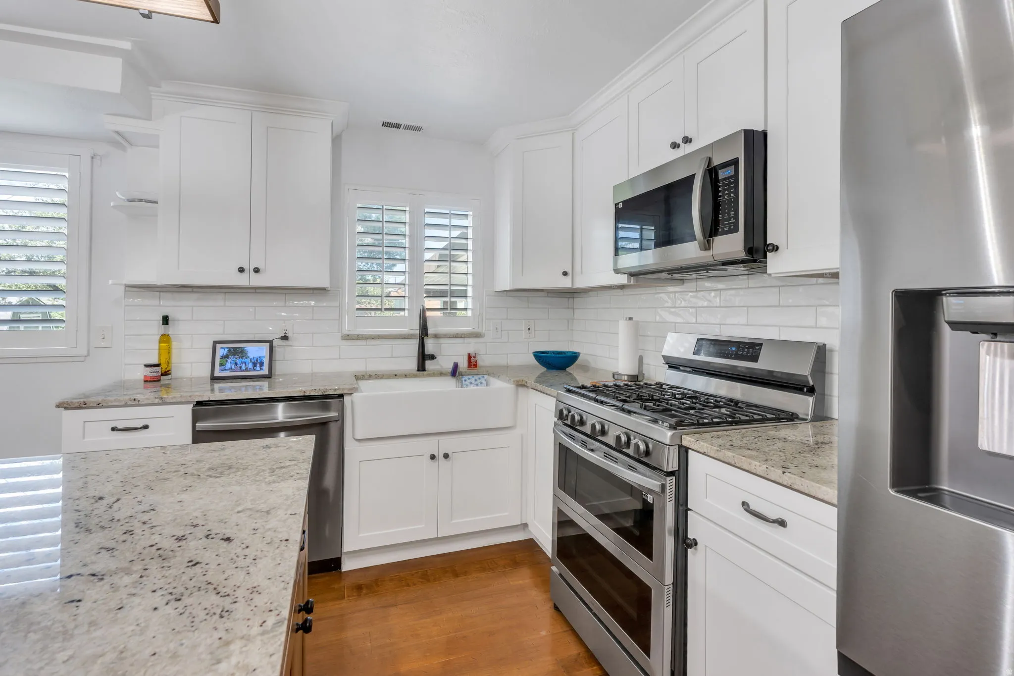Kitchen featuring white shaker cabinetry, stainless steel appliances, granite countertops, a farmhouse sink, and wood-finish flooring