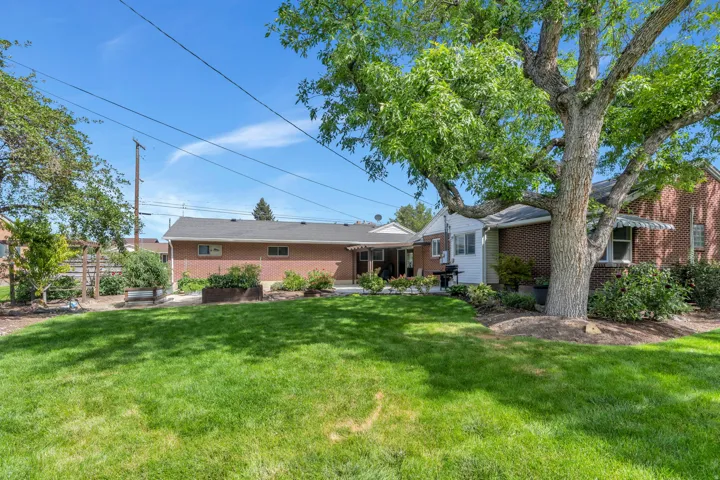 Expansive lawn with mature trees, a red brick exterior, and a covered patio area