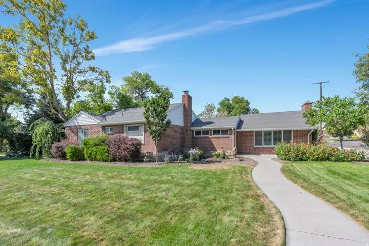 Brick exterior featuring multiple chimneys, a gabled roof, and a mature landscaped yard with a winding pathway