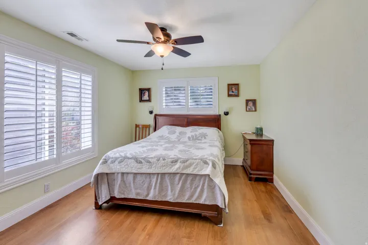 Hardwood flooring, two windows with plantation shutters, ceiling fan with integrated lighting, and light-toned walls