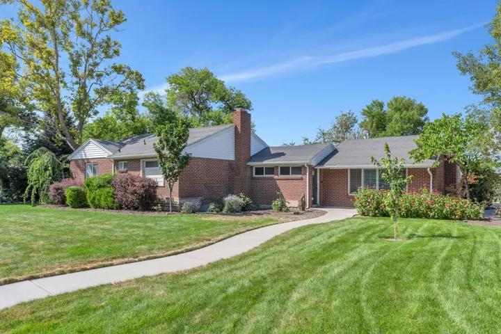 Brick exterior with white siding accents, mature trees, established landscaping, a concrete walkway, and a spacious lawn