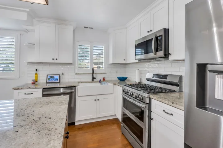 Kitchen featuring white shaker cabinetry, stainless steel appliances, granite countertops, a farmhouse sink, and wood-finish flooring
