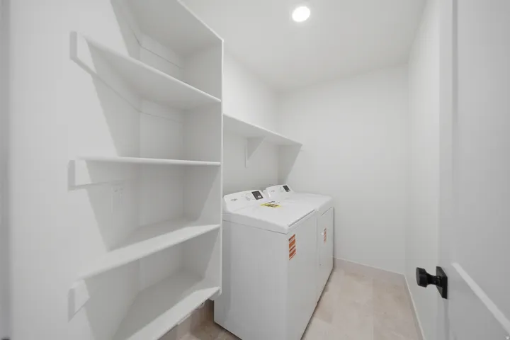 Dedicated laundry area featuring built-in shelving, overhead lighting, and tile flooring