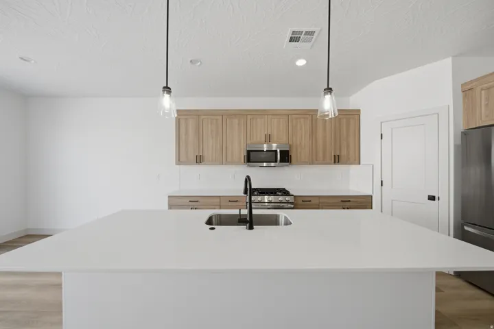 Expansive kitchen island with an undermount sink, stainless steel appliances, wood-finish cabinetry, and pendant lighting