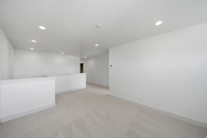 Recessed lighting illuminates a spacious room featuring light-toned carpeting and neutral wall finishes