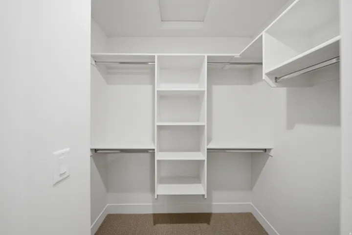 Walk-in closet with white shelving, multiple hanging rods, and a central shelving unit