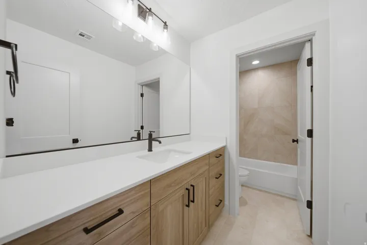 Wood-finish vanity with white countertop, undermount sink, and matte black fixtures