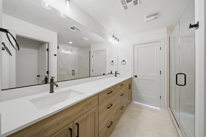 Extended vanity with dual sinks, a large mirror, and wood-finish cabinetry
