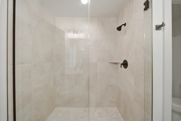 Glass-enclosed shower with large format wall tiles, a built-in shower shelf, and dark-finished fixtures