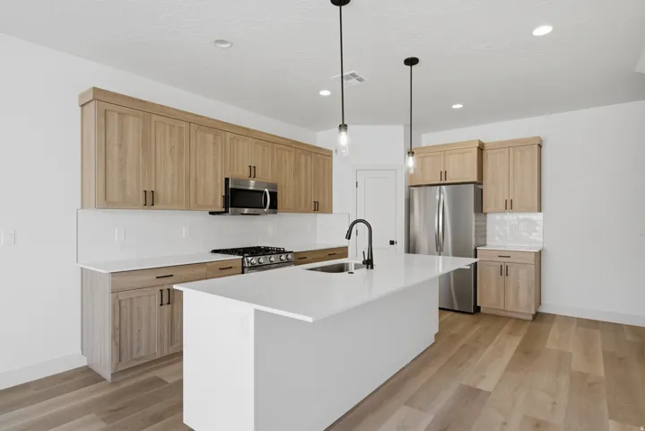 Kitchen featuring wood-finish cabinetry, stainless steel appliances, a center island with sink, white countertops, and pendant lighting