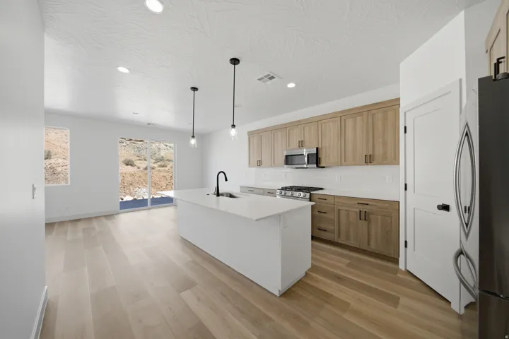 Kitchen featuring wood-finish cabinetry, stainless steel appliances, a white subway tile backsplash, and a large center island with a sink and pendant lighting