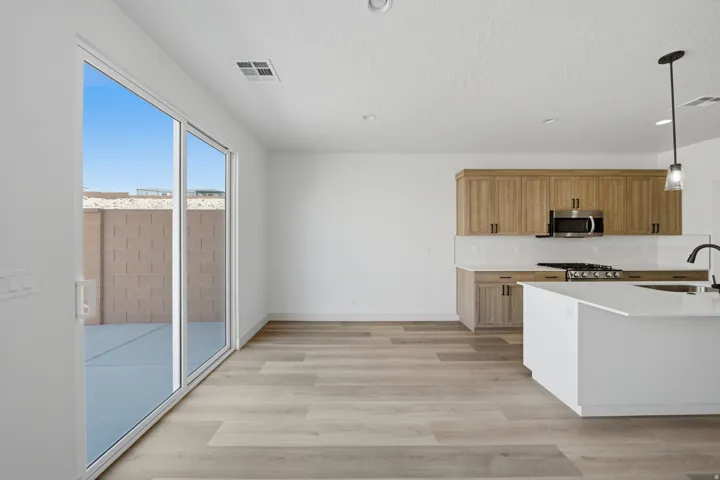 Open-concept living space with wood-finish flooring, a kitchen island with a sink, light wood cabinetry, and stainless steel appliances