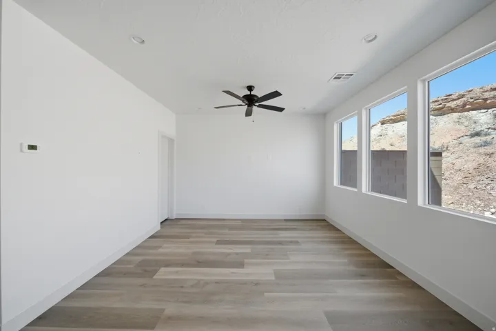 Recessed lighting, ceiling fan with light, wood-finish flooring, multiple windows, and a wall-mounted thermostat