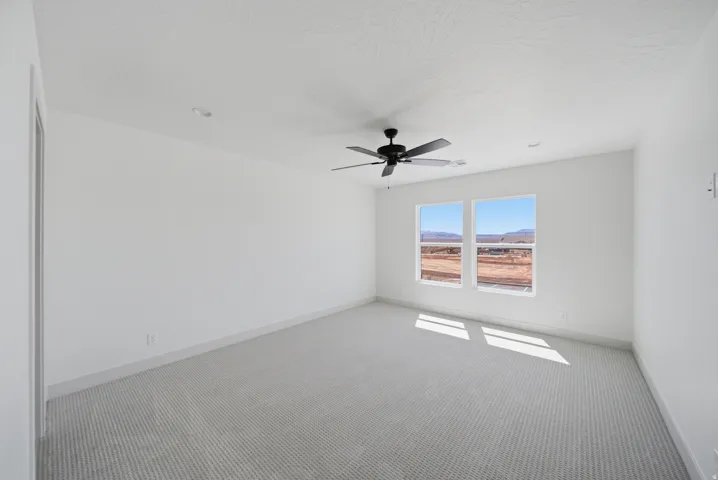 Spacious room with dual windows, textured carpet, and a ceiling fan