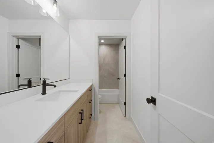 White countertop vanity with wood-finish cabinetry, matte black hardware, and integrated sink