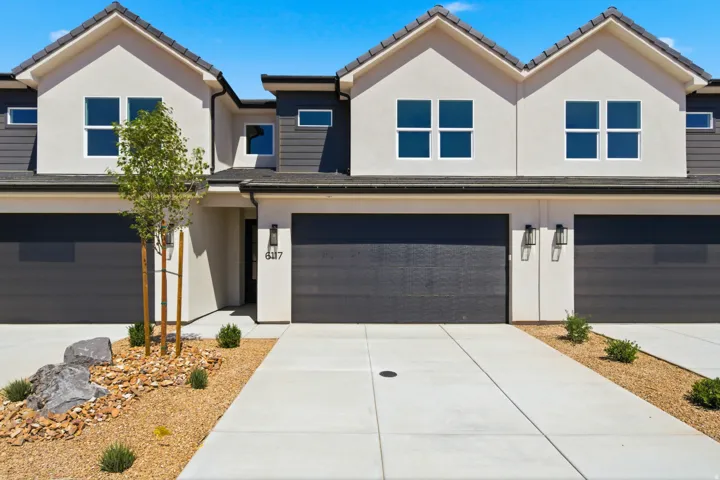 Stucco and siding exterior with dark garage doors, concrete driveways, and decorative rock landscaping