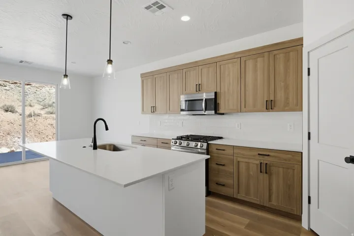 Modern kitchen featuring light wood-finish cabinetry, stainless steel appliances, a white tile backsplash, a large center island with a black faucet, and wood-finish flooring