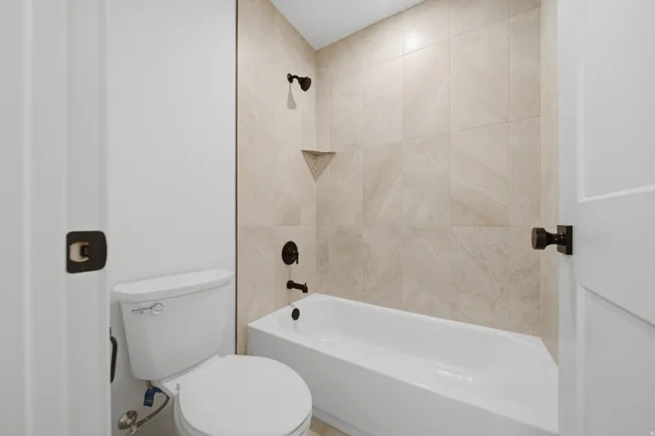 White porcelain bathtub with integrated shower, tiled surround, and matte black fixtures