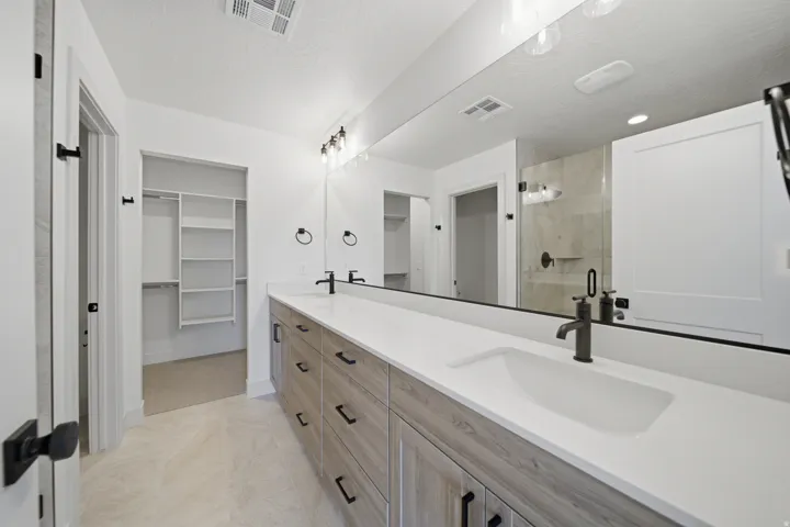 Dual vanity with integrated sinks, wood-finish cabinetry, matte black fixtures, and a spacious walk-in closet with built-in shelving
