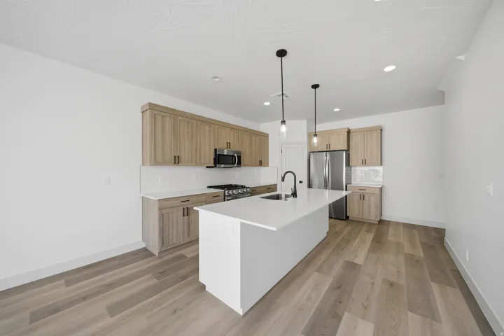 Kitchen featuring a central island with an integrated sink, wood-finish flooring, light-toned cabinetry, stainless steel appliances, and recessed lighting