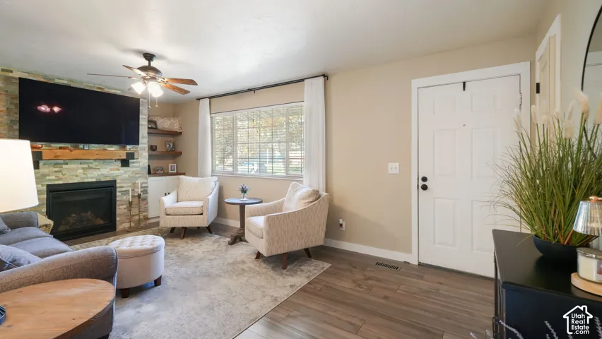 Living area featuring a stone-clad fireplace with wood mantel, built-in shelving, wood-finish flooring, and a ceiling fan with integrated lighting