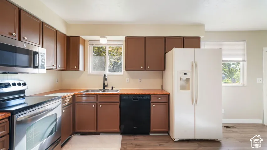 Kitchen featuring wood-finish cabinetry, stainless steel appliances, a double basin sink, and wood-finish flooring