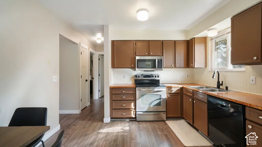Kitchen featuring wood-finish flooring, brown cabinetry, stainless steel appliances, and a window above the sink